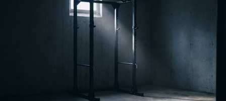 An empty power rack in a dim basement, lit by a single small window.